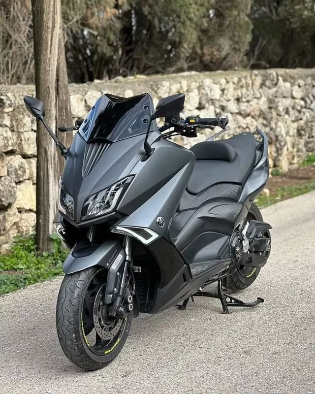 a black motorcycle parked on the side of a road next to a stone wall and trees