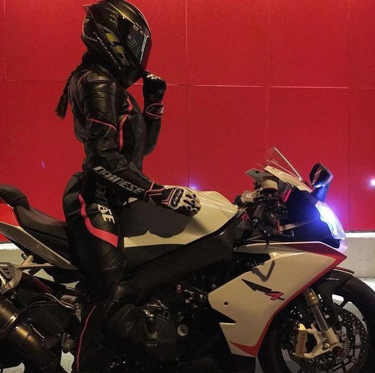 a man dressed in black riding on the back of a white and red motorbike