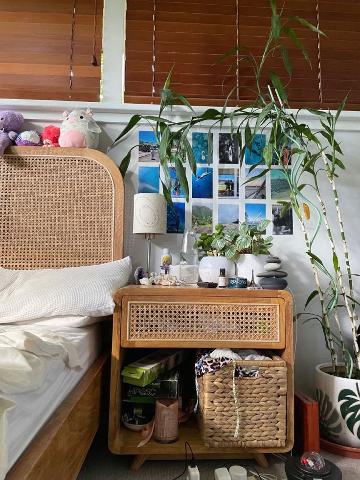 a wicker side table with baskets and plants on it in front of a bed