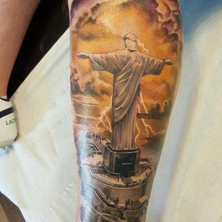 a person with a tattoo on their arm that has the statue of jesus in it