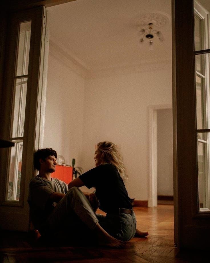 a man and woman sitting on the floor in front of an open door looking at each other