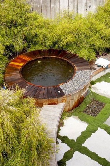 an outdoor hot tub in the middle of a garden with grass and rocks around it