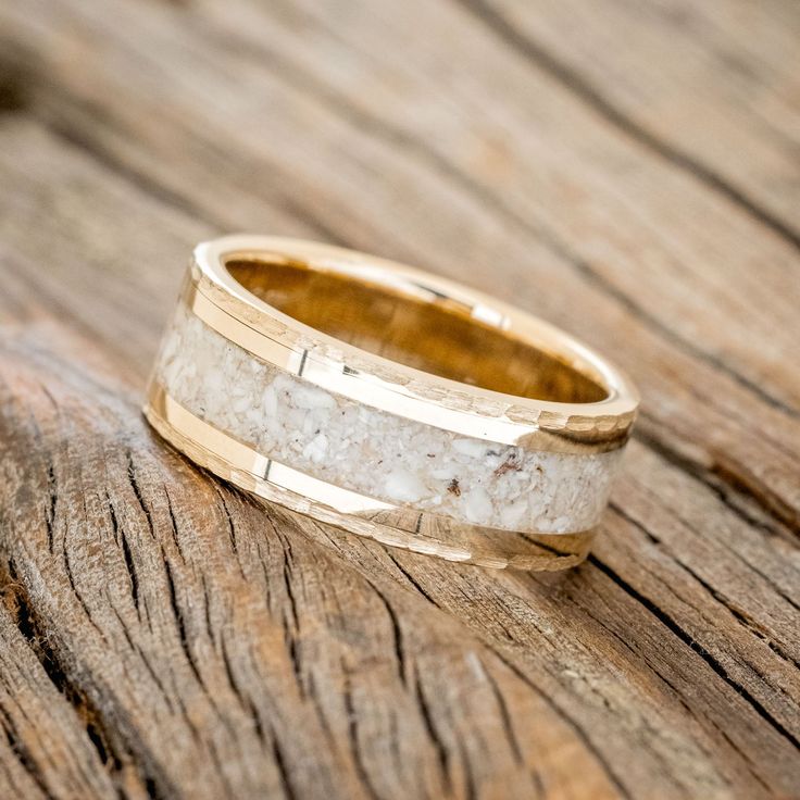 a wedding band that has been made from gold and white marble, on top of a wooden surface