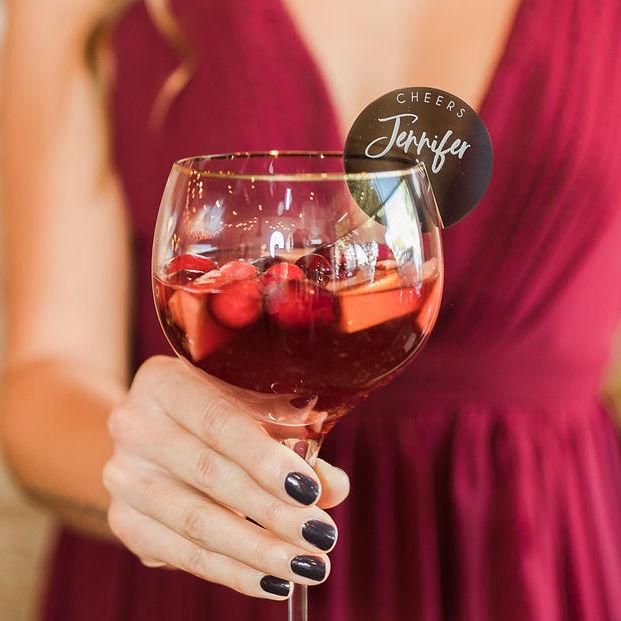 a woman in a red dress holding up a wine glass with fruit inside and label on it