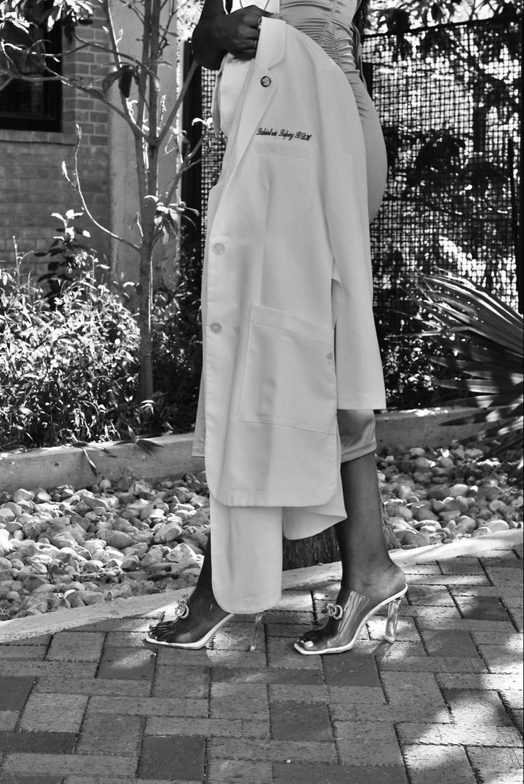 a black and white photo of a woman in a robe on the sidewalk holding an umbrella