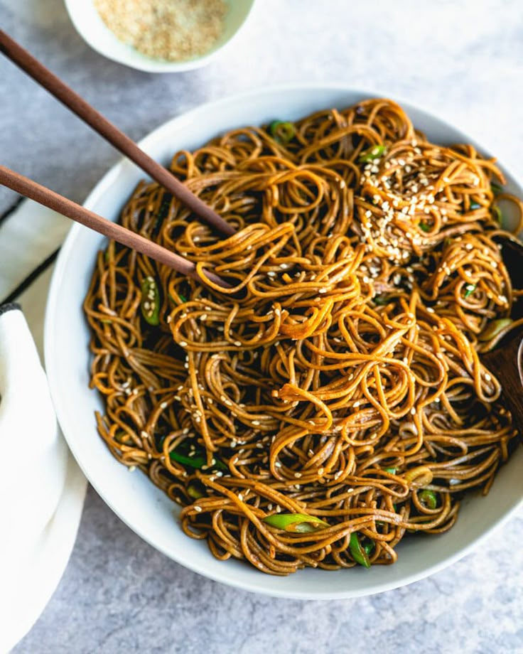 a bowl filled with noodles and chopsticks on top of a white tablecloth