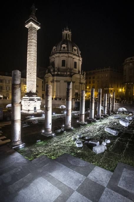 an empty courtyard at night with stone pillars and grass in the foreground, lit up by street lights