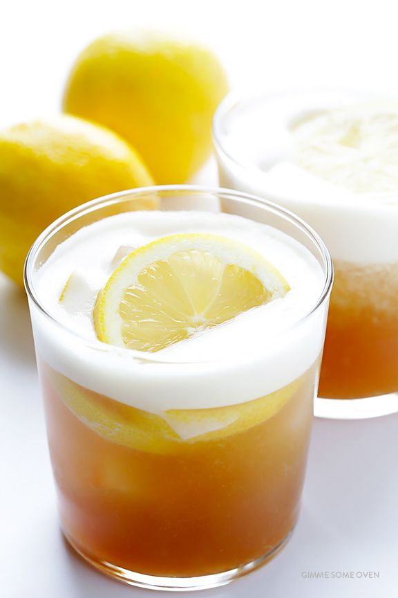 two glasses filled with liquid and lemons next to each other on a white surface