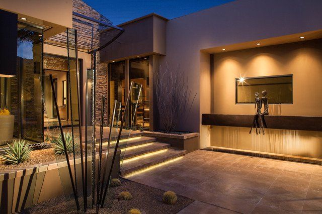 a modern home at night with lights on the front door and stairs leading up to it