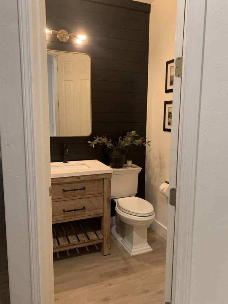 a white toilet sitting inside of a bathroom next to a wooden sink vanity and mirror