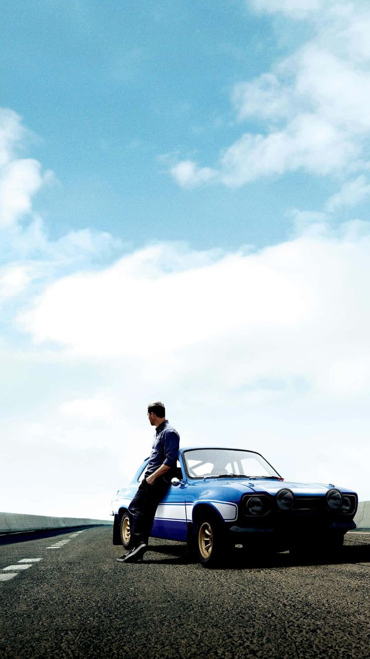 a man sitting on the hood of a blue car in the middle of an empty road