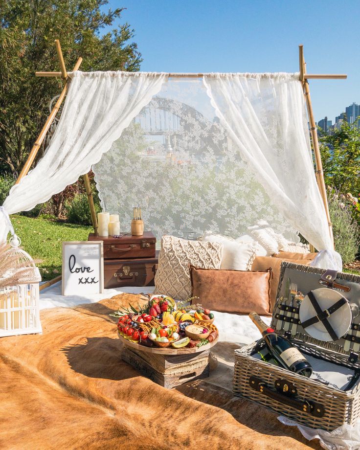 an outdoor picnic area with food on the table and in front of it is a white drape