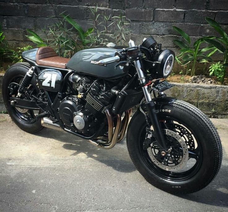 a black motorcycle parked in front of a brick wall next to some plants and trees