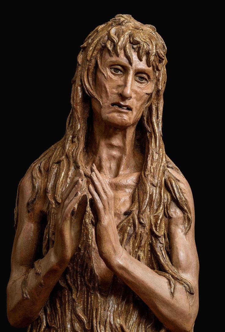 a statue of a man with long hair holding his hands in front of his chest