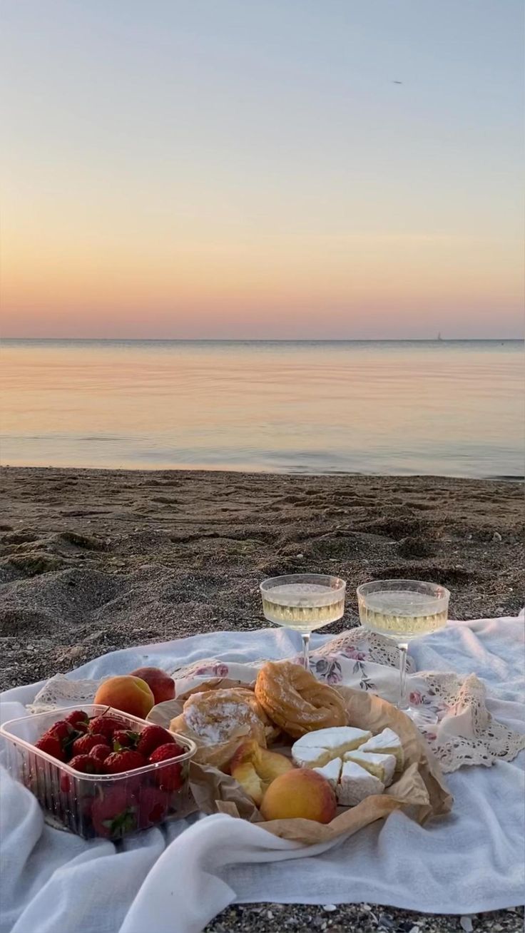 a picnic on the beach with fruit and bread in front of the ocean at sunset