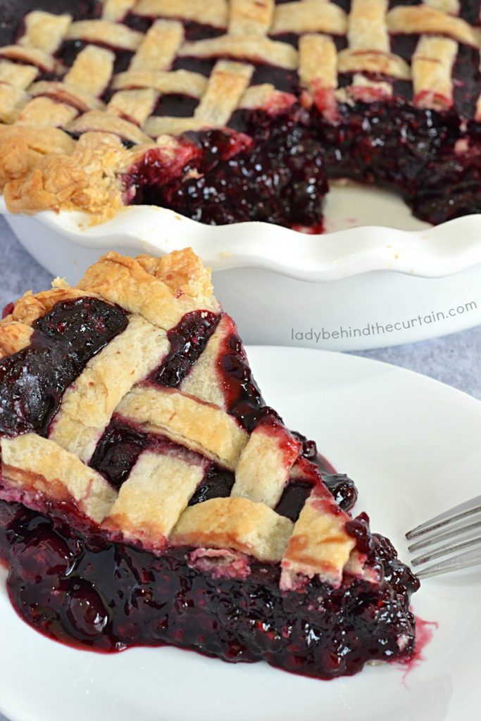 a slice of blueberry pie on a white plate with a fork next to it