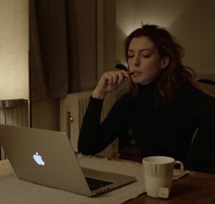 a woman sitting at a table with an apple laptop in front of her, while looking at the screen