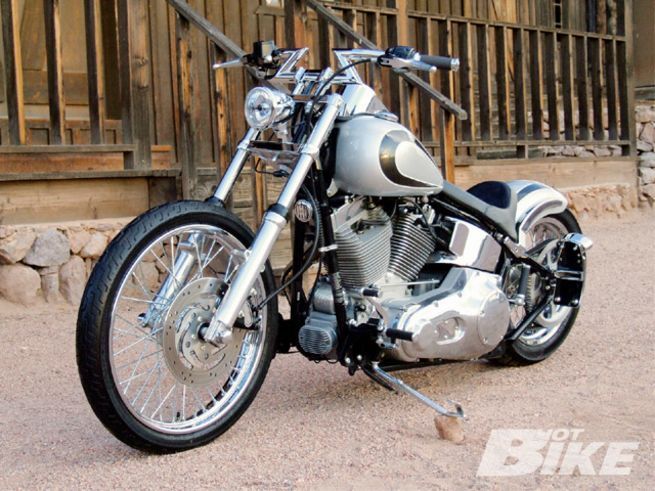 a silver motorcycle parked on top of a dirt road next to a wooden fence and building