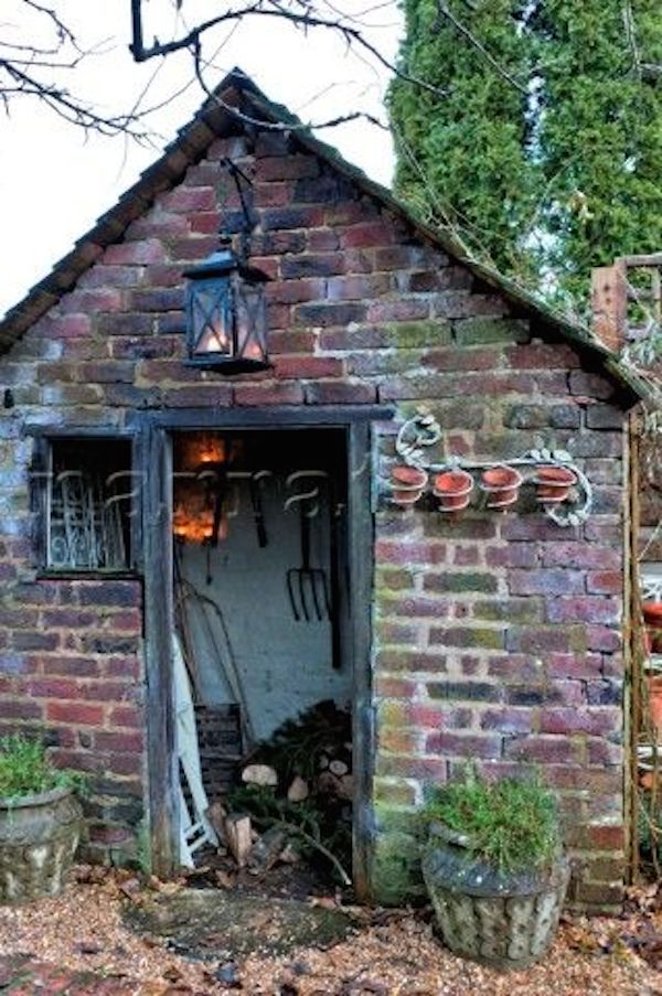 an old brick building with gardening tools in the doorway and pots on the ground next to it