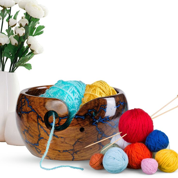 a wooden bowl filled with balls of yarn and crochet hooks next to white flowers