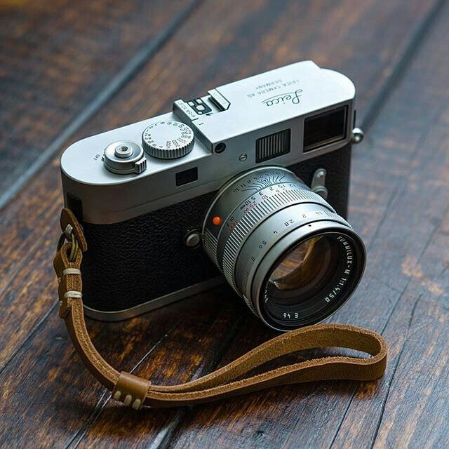 a camera sitting on top of a wooden floor next to a brown leather strap,