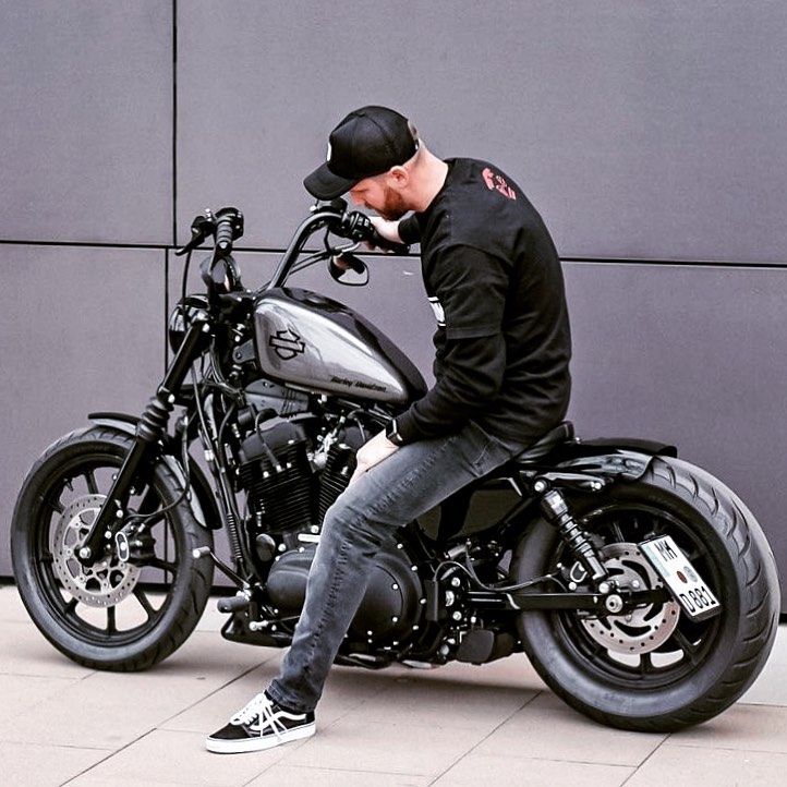 a man sitting on top of a motorcycle next to a gray wall in front of a building