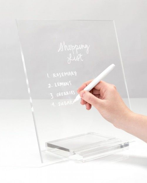 a person writing on a clear acrylic sign with a white pen in their hand