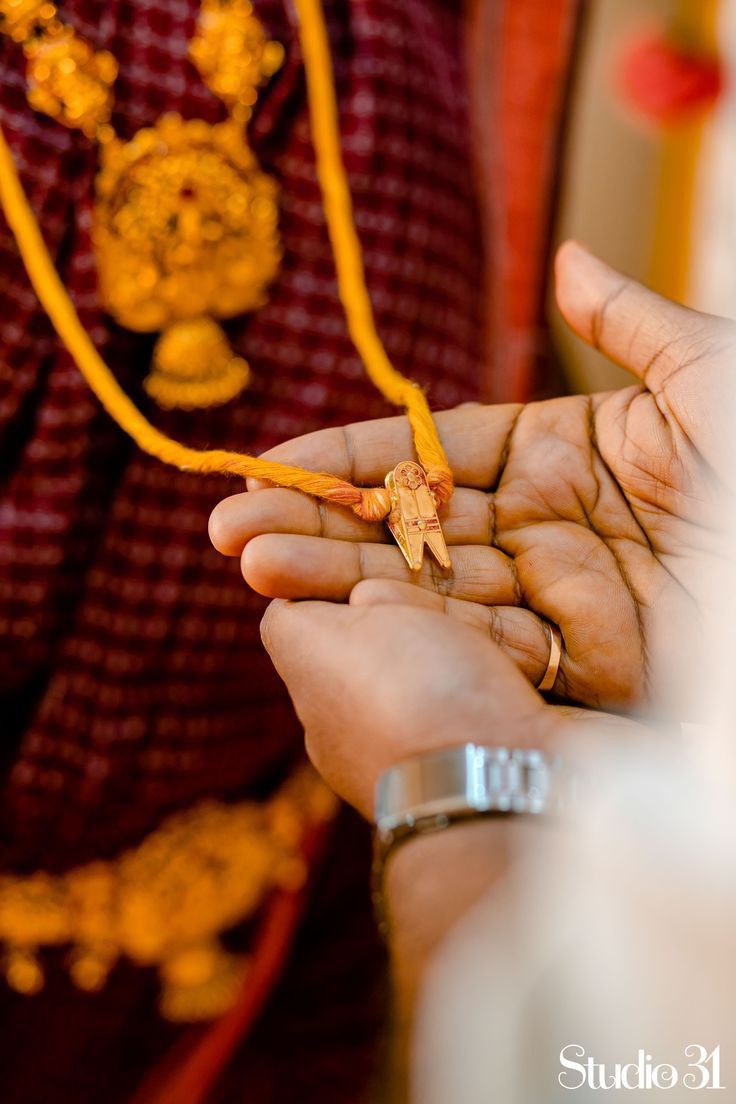 a person holding something in their hand while wearing a necklace and bracelet with an orange flower on it