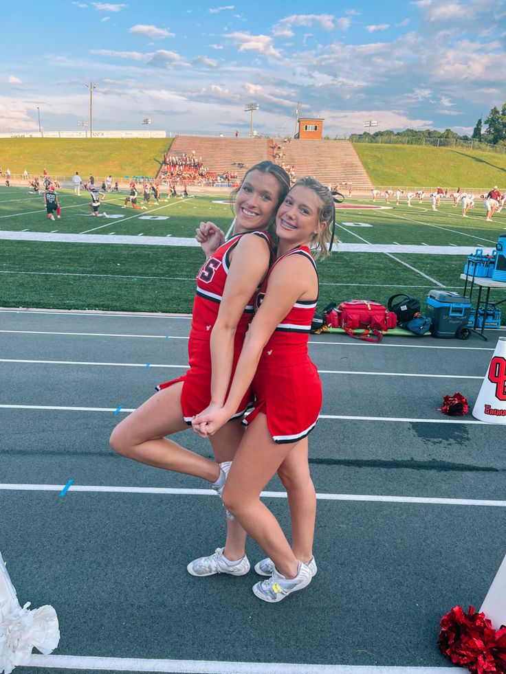 two cheerleaders hugging each other in the middle of an outdoor track with people watching