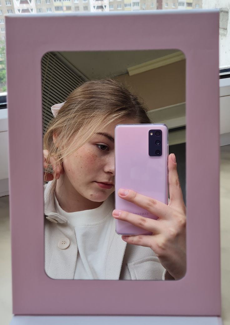 a woman holding up her cell phone in front of a pink and white box with a window