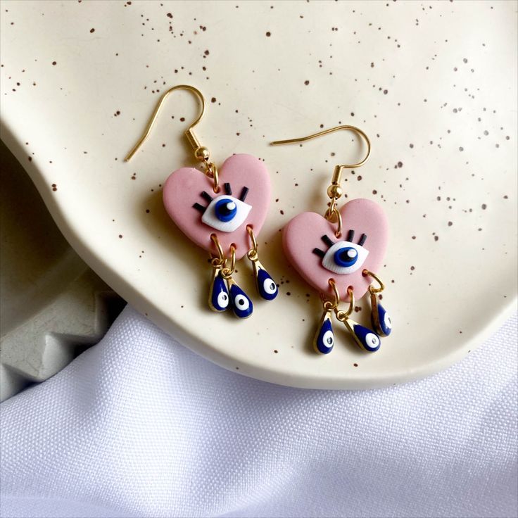 two pink heart shaped earrings with blue eyes on top of a white plate next to a napkin