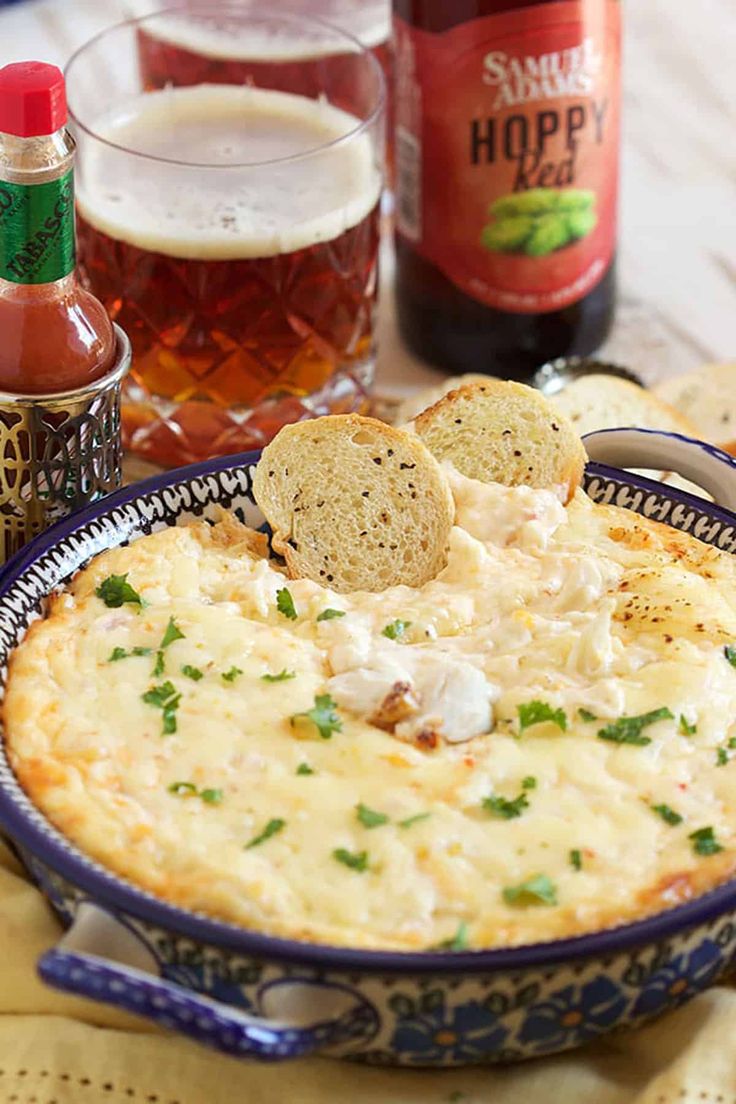 a bowl of dip with crackers and beer in the background