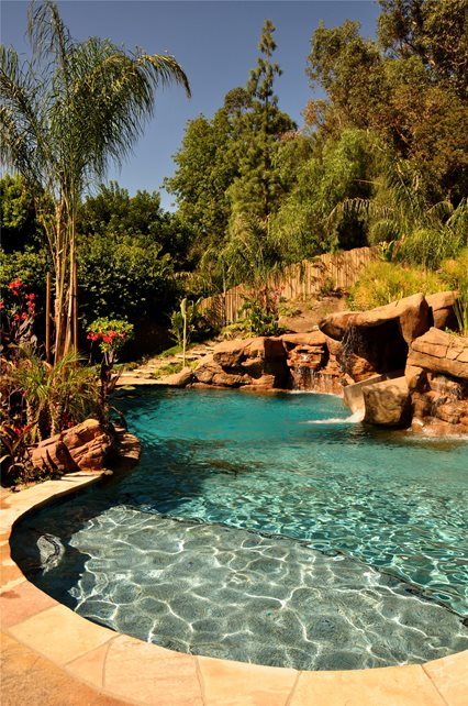 an outdoor swimming pool surrounded by trees and rocks, with a waterfall in the middle