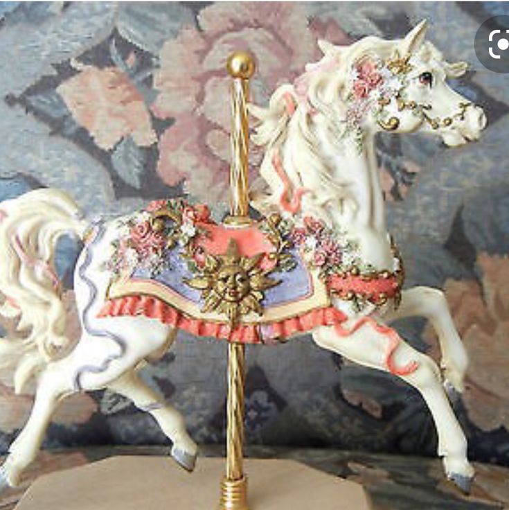 a white and pink carousel horse on a stand in front of a floral wallpaper