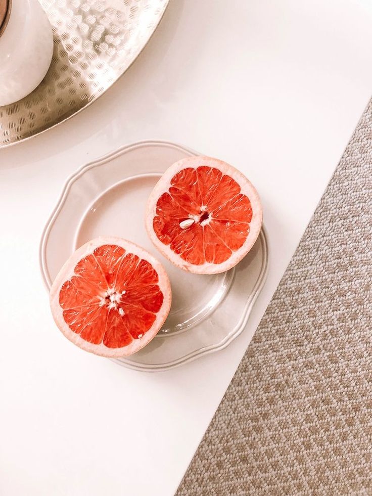 two halves of grapefruit on a plate next to a cup and saucer