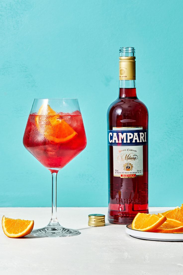 a bottle of campari next to a glass with orange slices on the rim and a plate