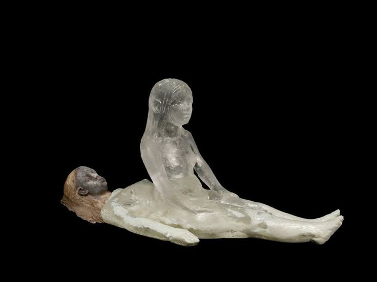 a sculpture of a woman laying on the ground next to a small statue of a man