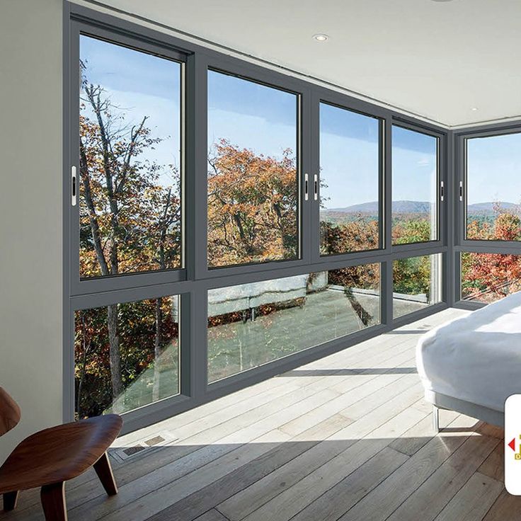 a bedroom with large windows and wooden flooring, overlooking the trees in the distance