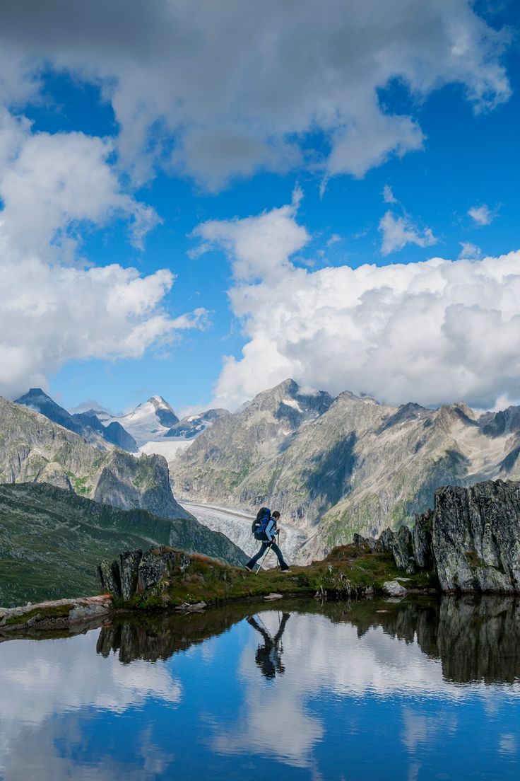 a man standing on top of a mountain next to a lake with mountains in the background