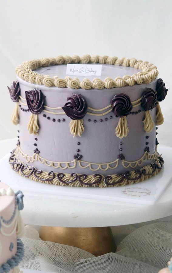 a purple and gold decorated cake sitting on top of a white table next to other cakes