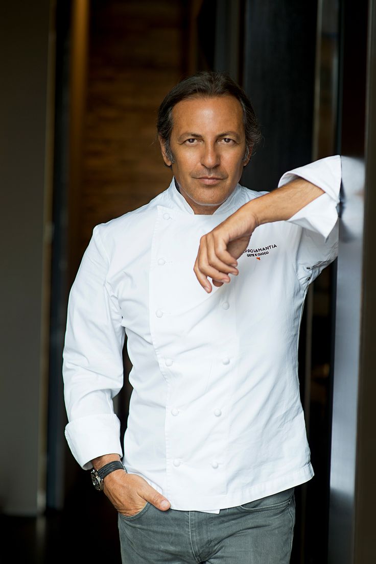 a man in a chef's coat leaning against a wall and pointing at the camera