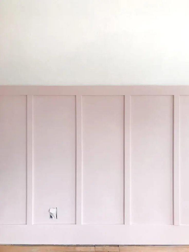 an empty room with white paneling and wood flooring on the walls, painted in pale pink