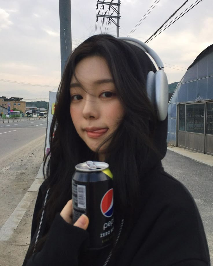 a woman with headphones holding a can of pepsi