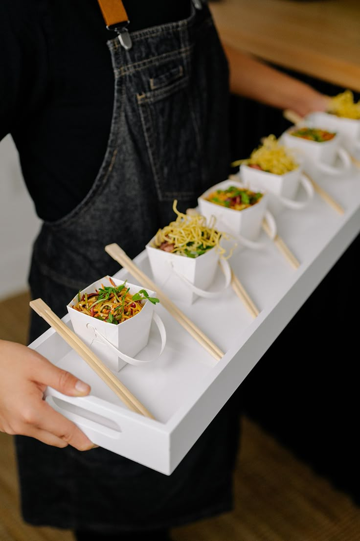 a person holding a tray with food on it and chopsticks in their hands