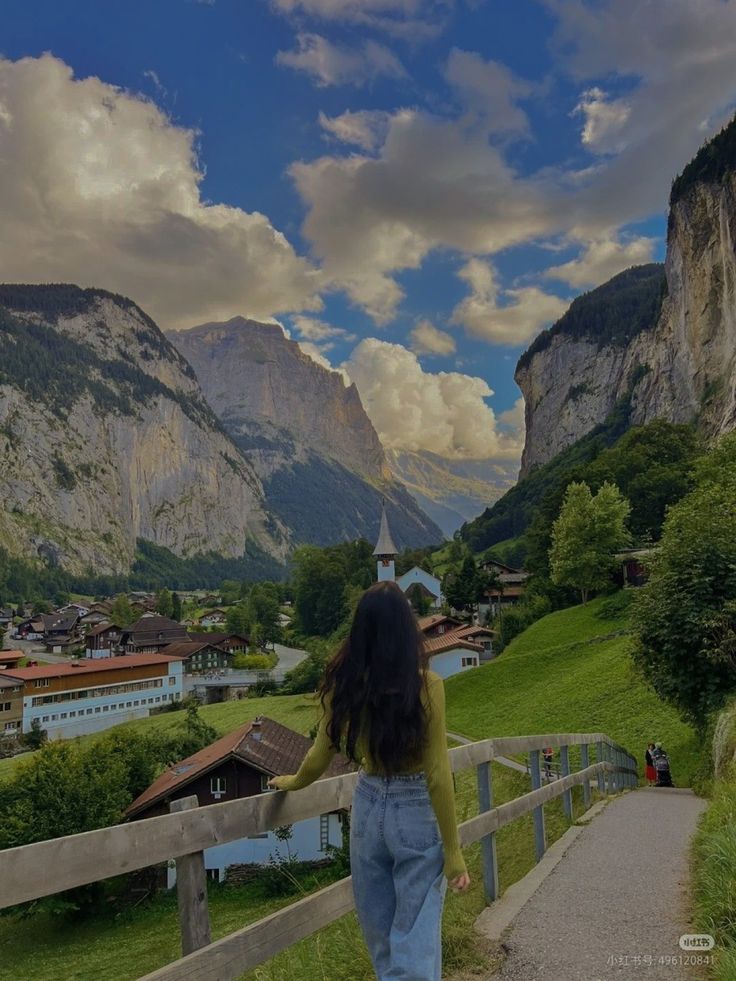 a woman walking down a path in the mountains with her back turned to the camera