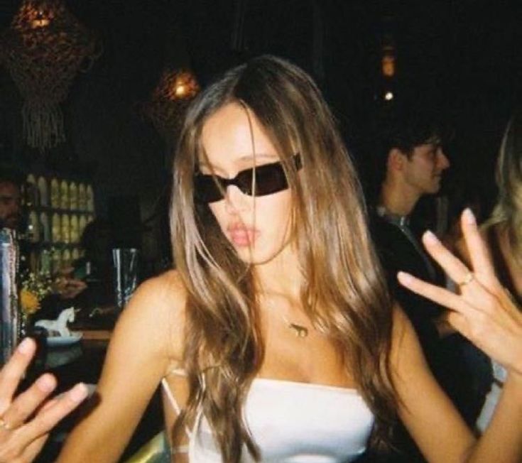 a woman wearing sunglasses standing in front of a bar with her hands out to the side