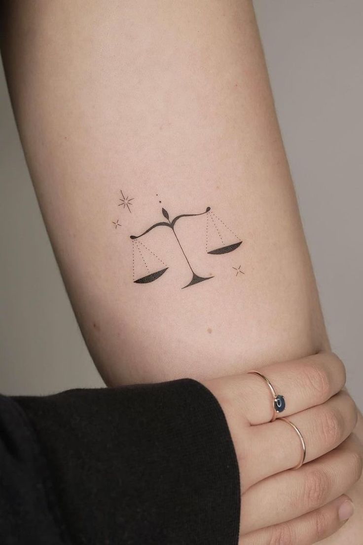 a woman's arm with a tattoo on it that has an image of a scale and stars