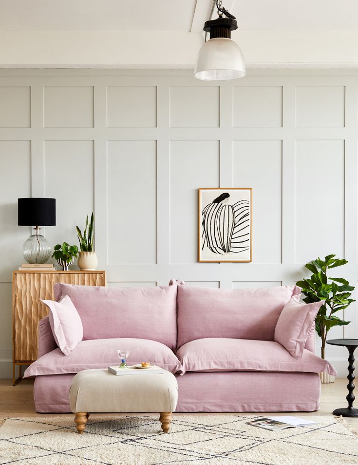 a living room with a pink couch and ottoman in front of a white paneled wall