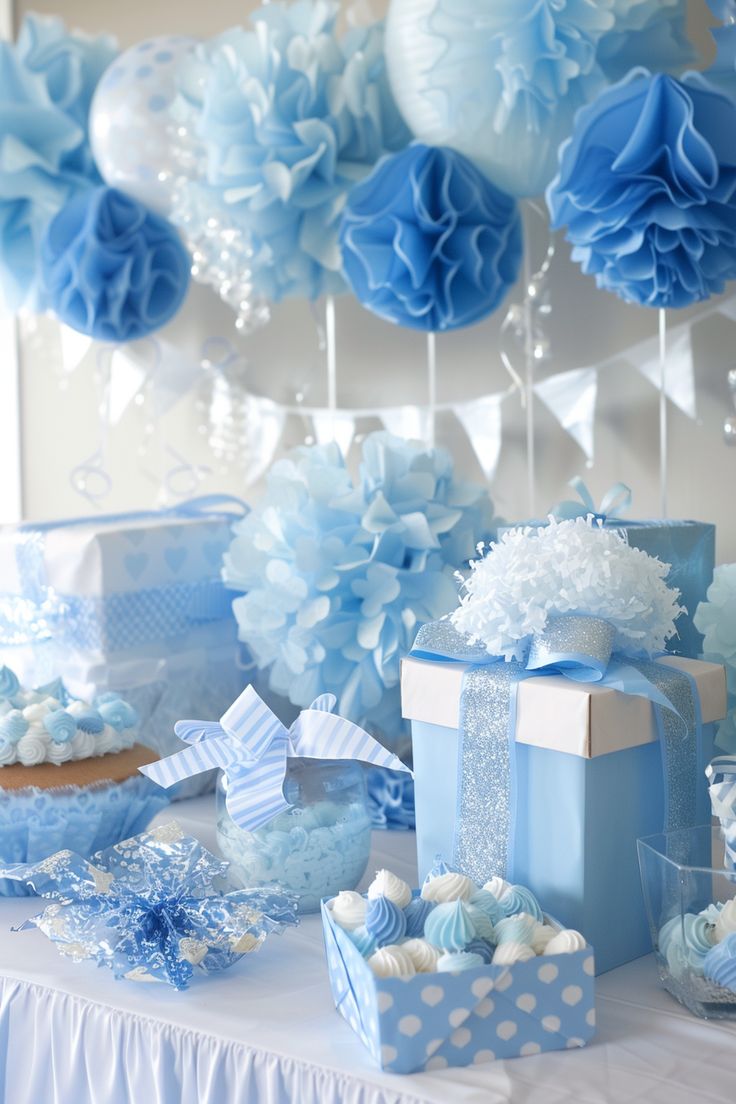 a table topped with blue gift boxes and paper pom poms hanging from the ceiling