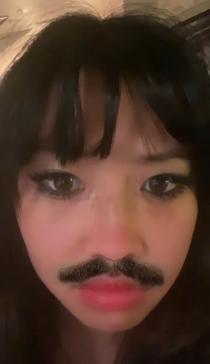 a woman with long black hair and a moustache on her face is taking a selfie